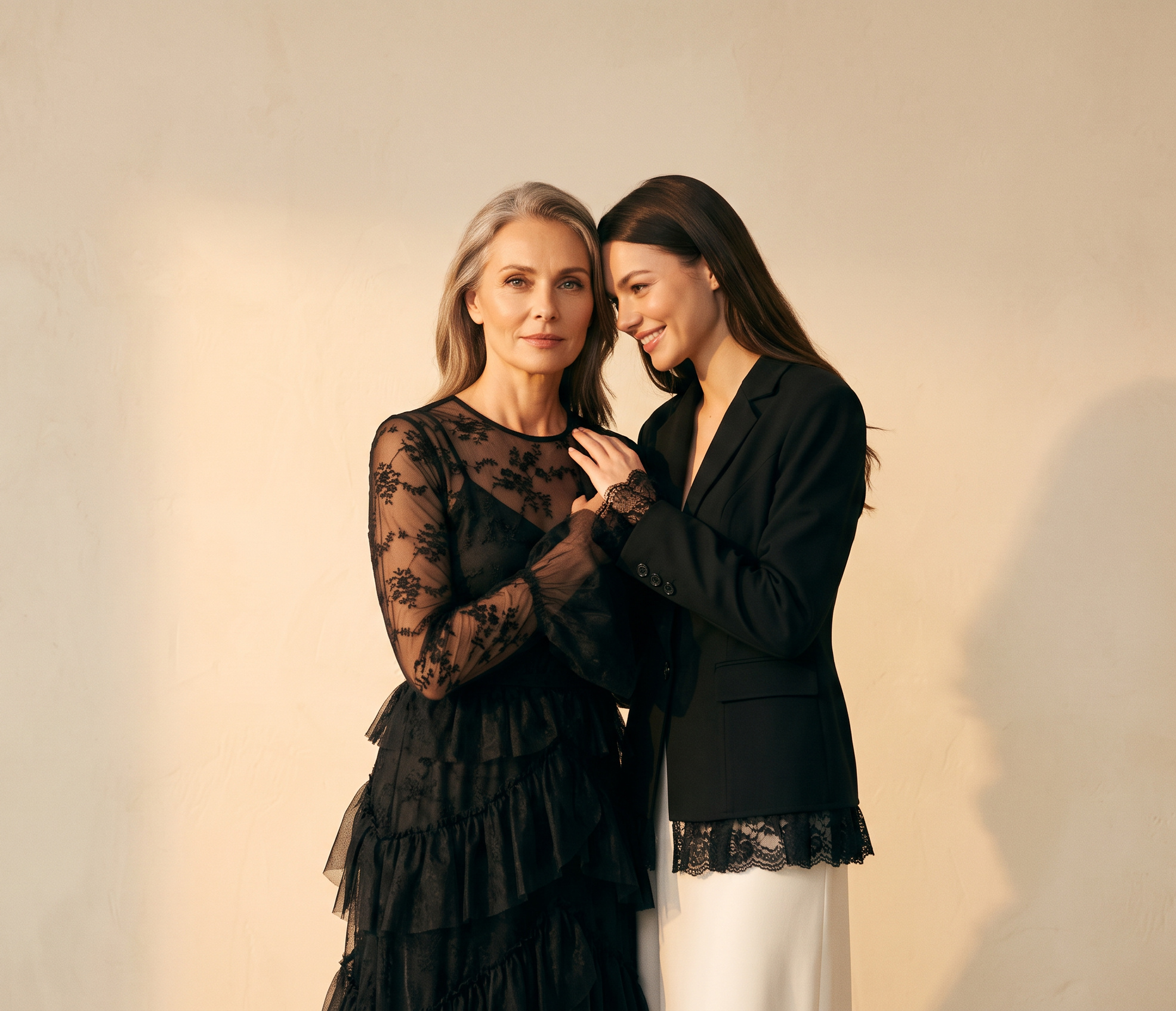 KEEE F/W 2026 — a mother in the embroidered mesh tiered maxi dress leaning close to her daughter in the lace-trimmed tailored blazer and ivory skirt